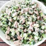 closeup of all green salad with ham in a white salad bowl with fresh dill on the side