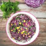Red cabbage and mango slaw in a white salad bowl with pink rim.