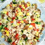 sausage and rice salad in a blue salad bowl with lemon wedges and cucumber on the side