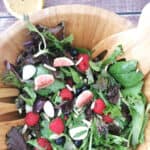 spring vegetable and berry salad mixed in a large wooden salad bowl.
