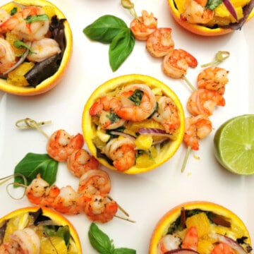 Shrimp Salad in Orange Peel on a white plate with lime and fresh basil