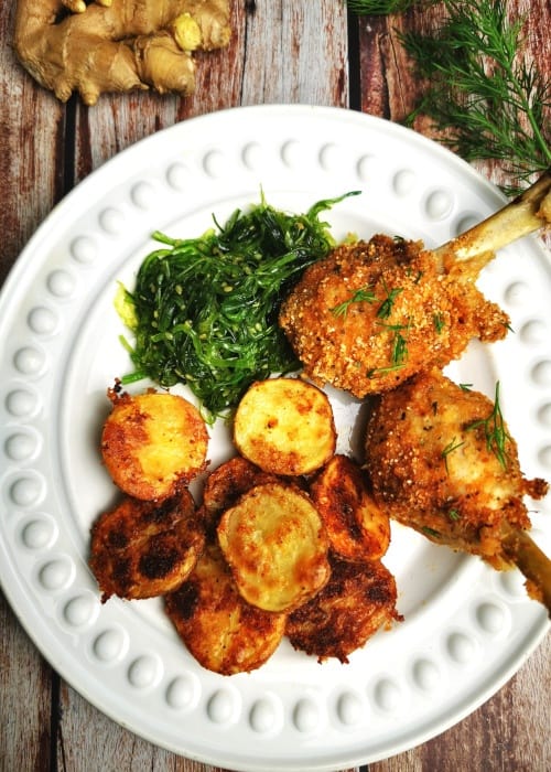 Baked chicken drumsticks on white serving plate with baked potatoes and seaweed salad