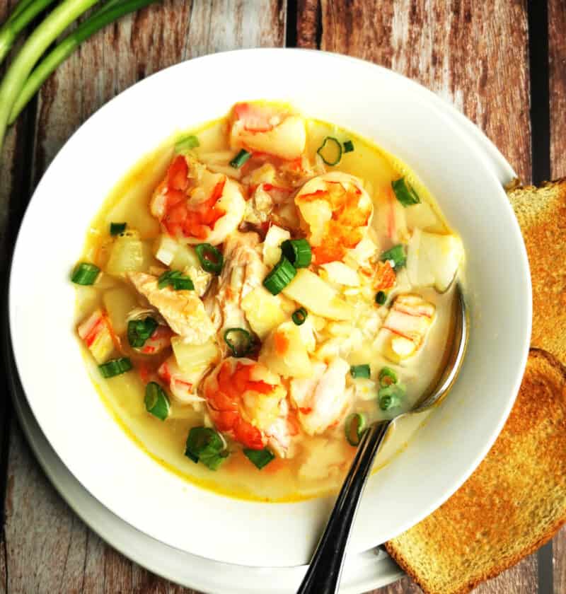 seafood soup in white bowl with tablespoon with green onion and toast on the side