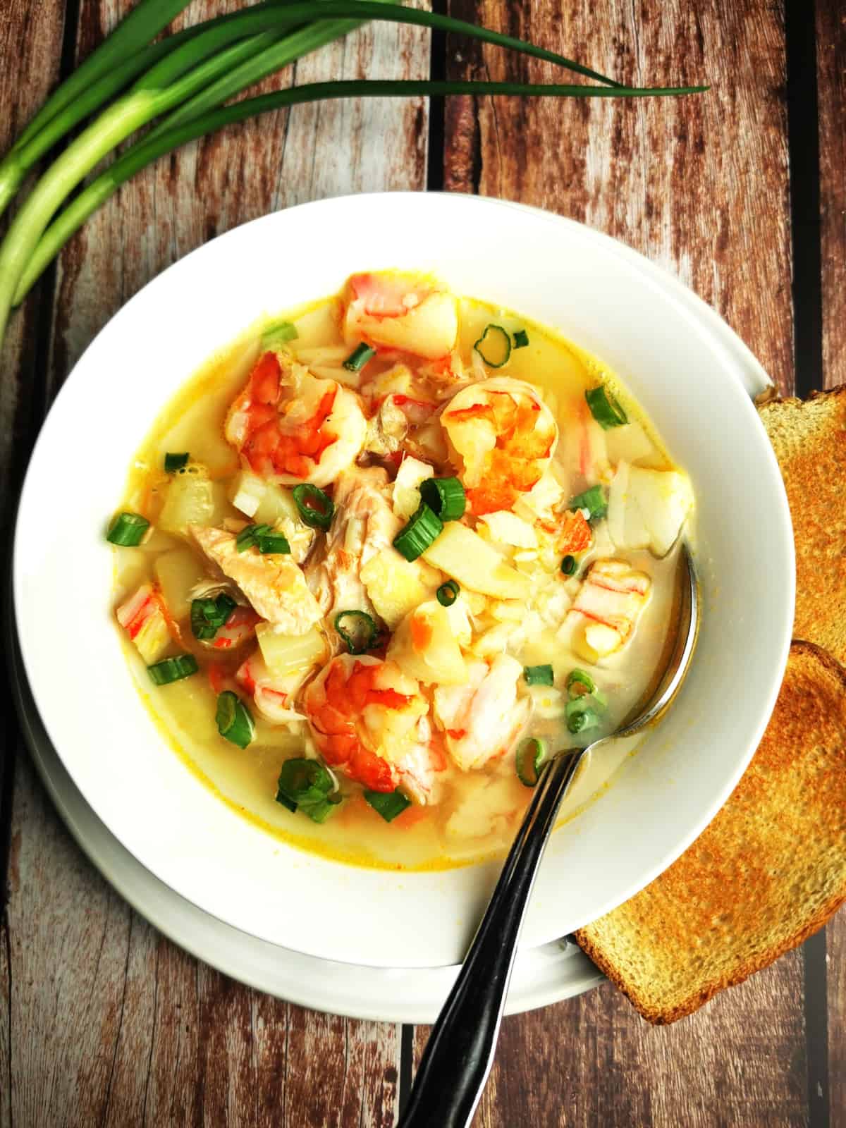 seafood soup in white bowl with tablespoon with green onion and toast on the side