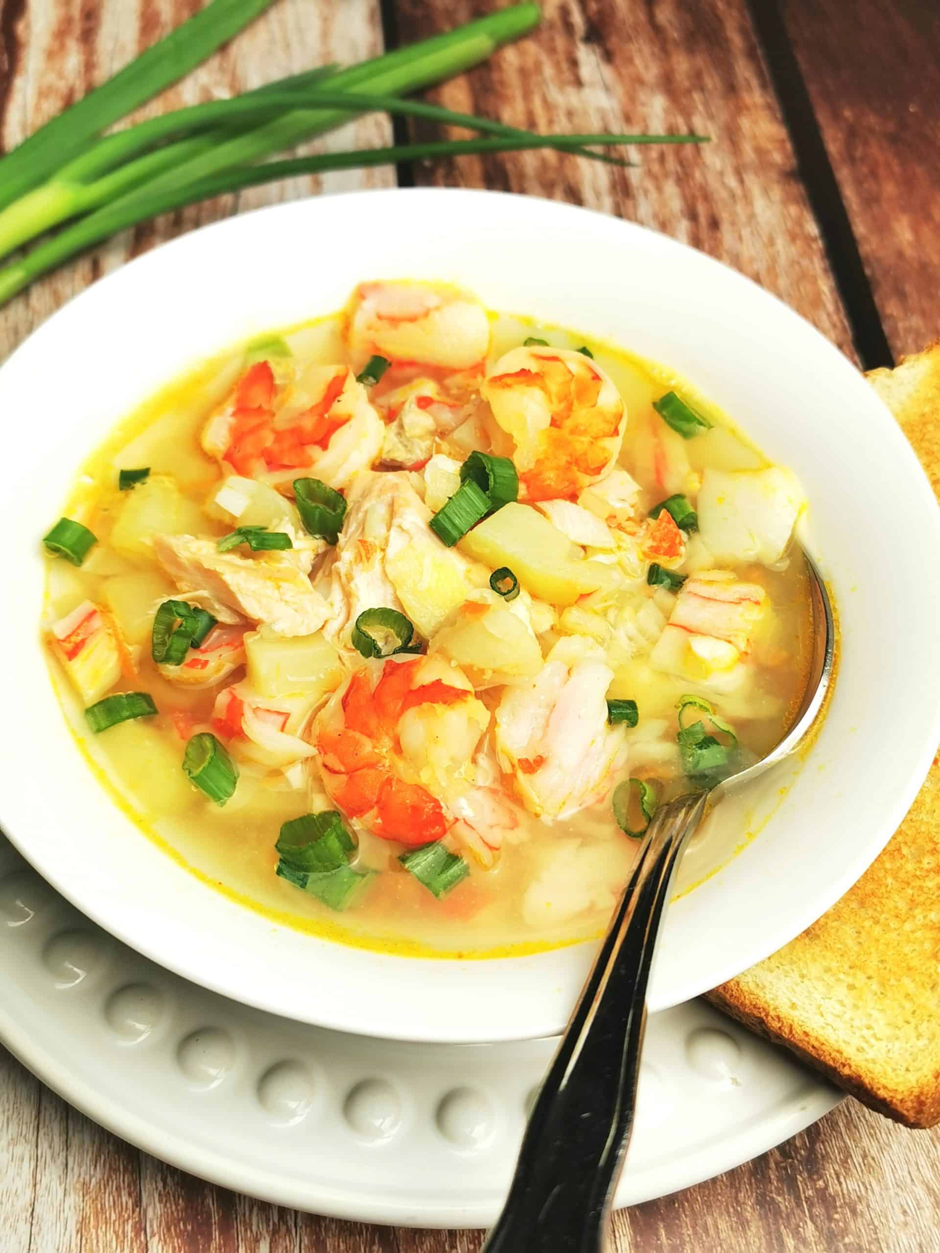 Seafood Soup in white bowl with green onion and toast on the side