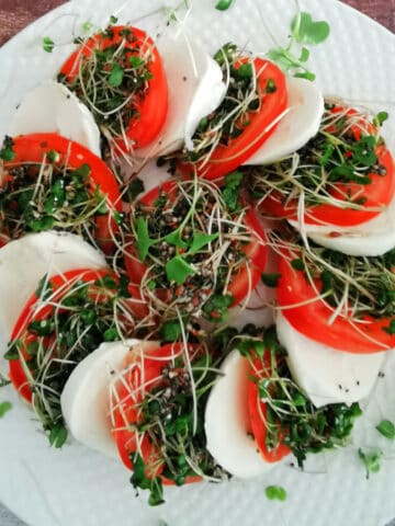 Caprese salad with microgreens on white plate.