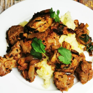 Stir-Fried Chicken Thighs on a white serving plate over mashed potatoes