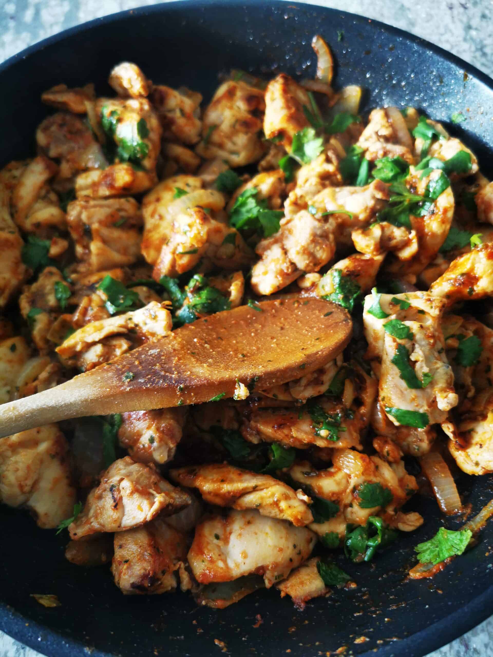 Stir-Fried Chicken Thighs in pan over stove with wooden spoon stir in cilantro