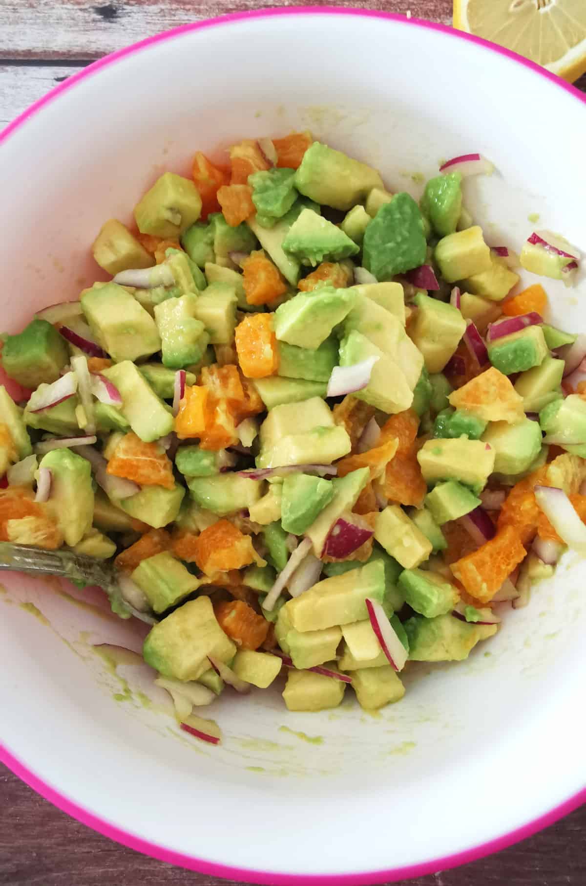 citrus avocado salad in white and pink bowl with lemon on the side