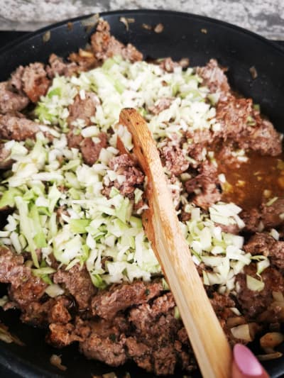 adding cabbage to ground beef and stirring with wooden spoon on stovetop