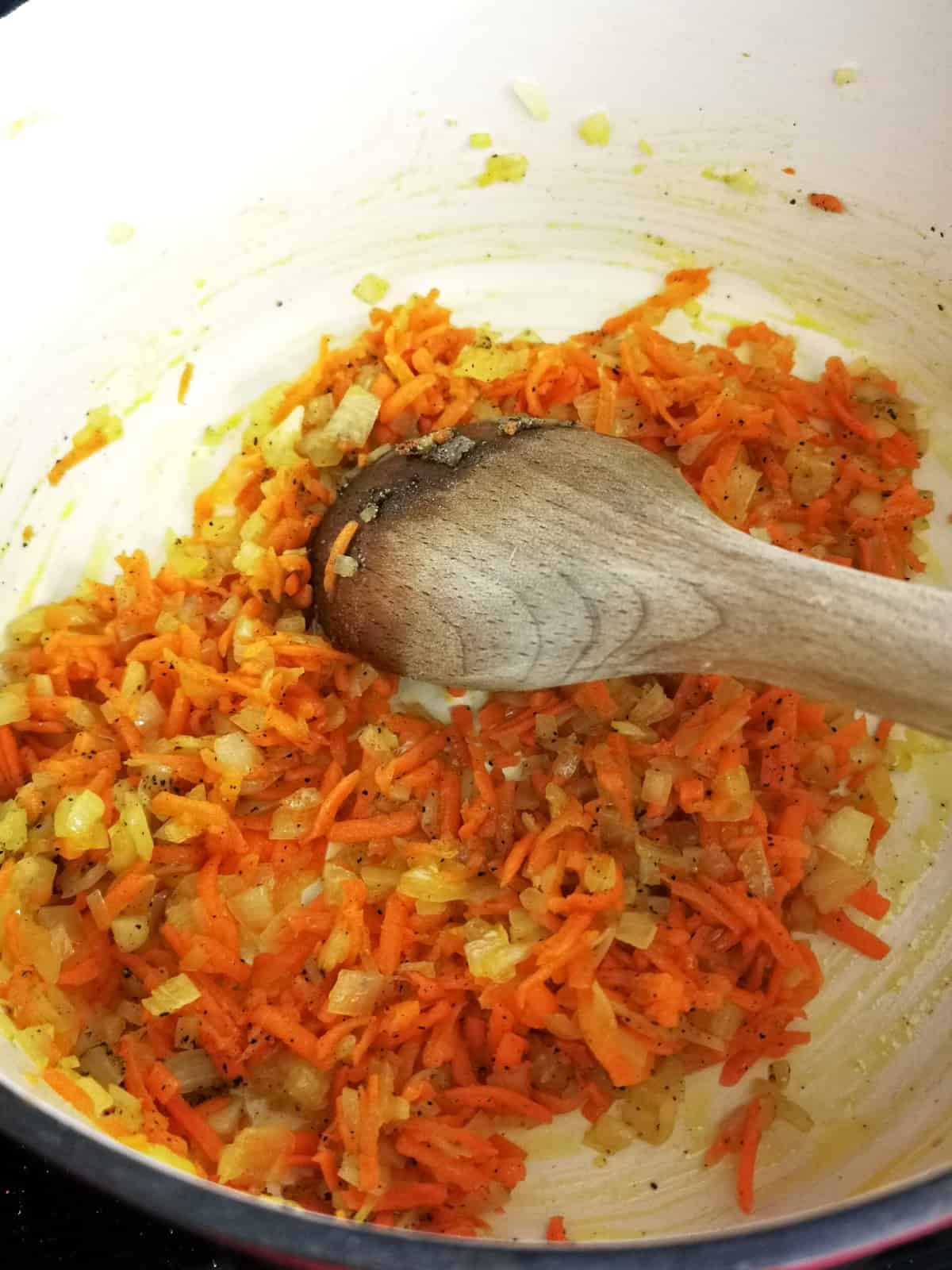 onion and grated carrot frying in dutch oven, stirred with a wooden spoon