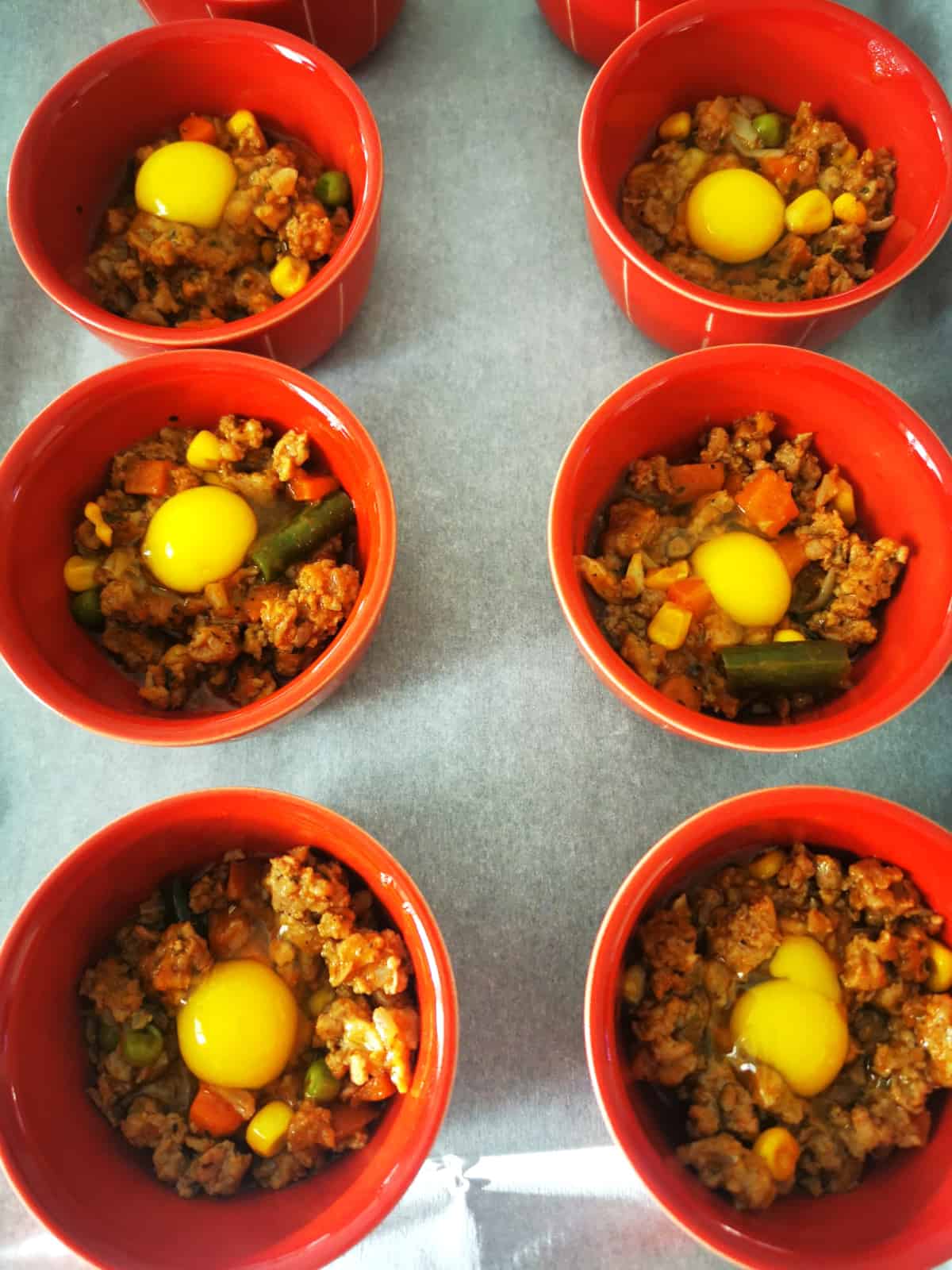 ground meat placed in small red bowls with quail egg cracked into each bowl