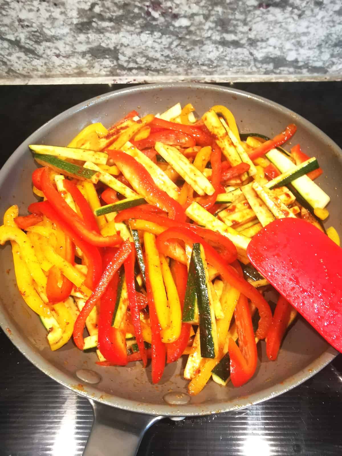 onion, bell peppers and zucchini sauteed in frying pan with red spatula