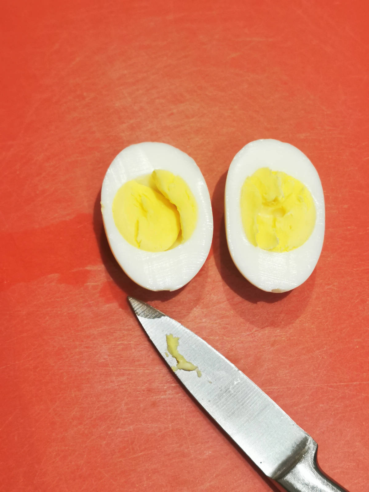 one egg sliced in half on a red cutting board with knife on the side