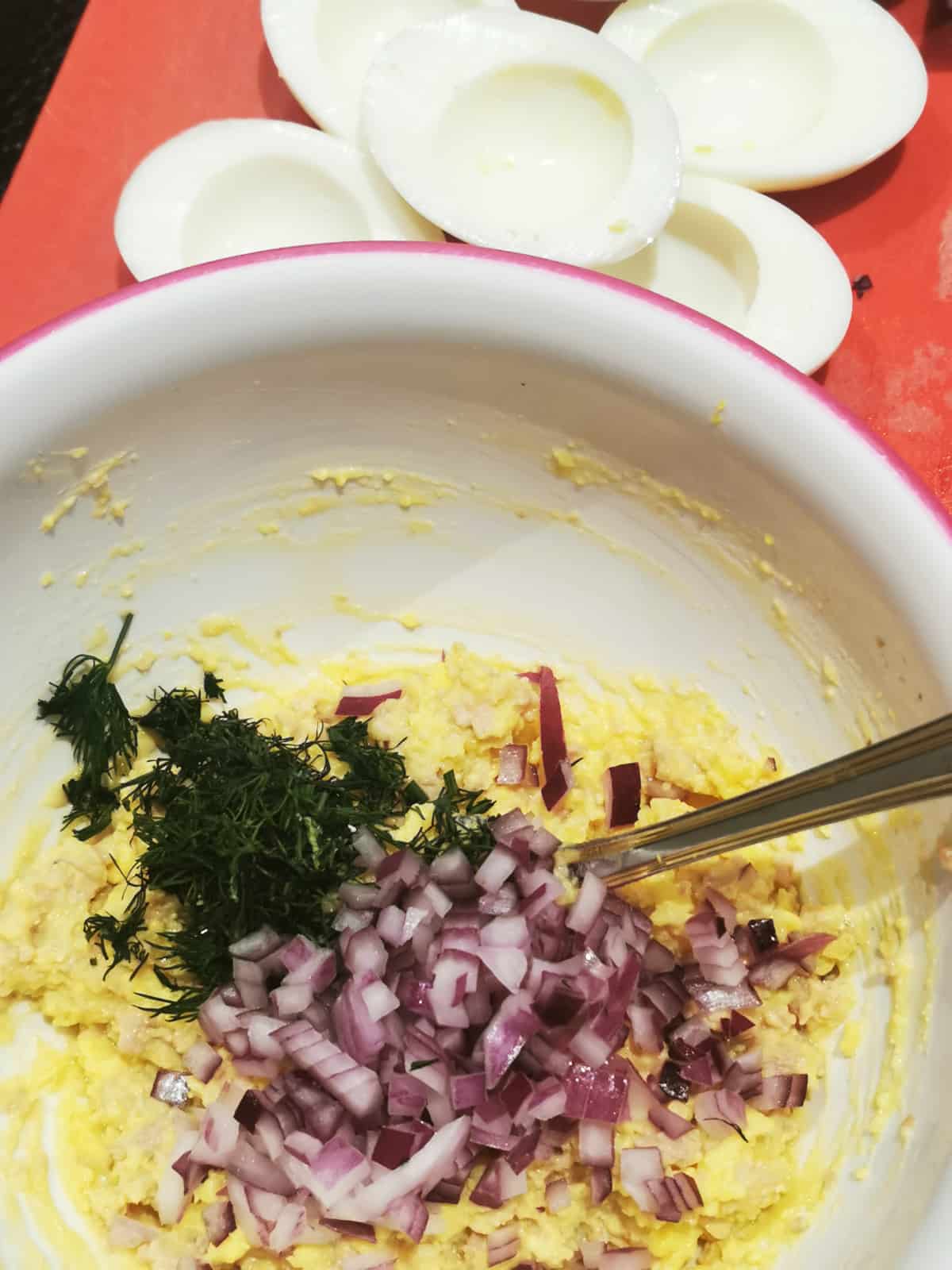 red onion and dill stirred into a pink bowl with cod liver and egg yolks