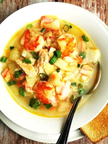 seafood soup recipe in white bowl with green onion and toast on the side