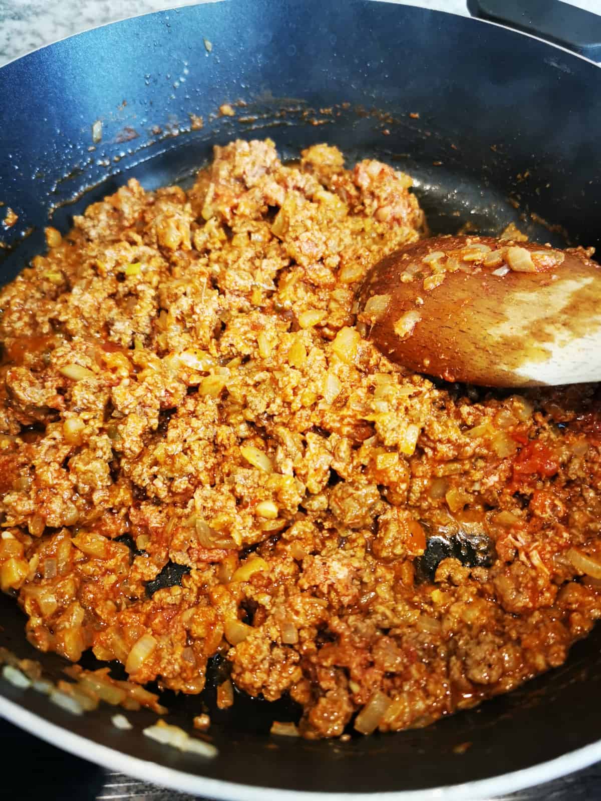 seasoned ground beef sauteed in a skillet with a wooden spatula.