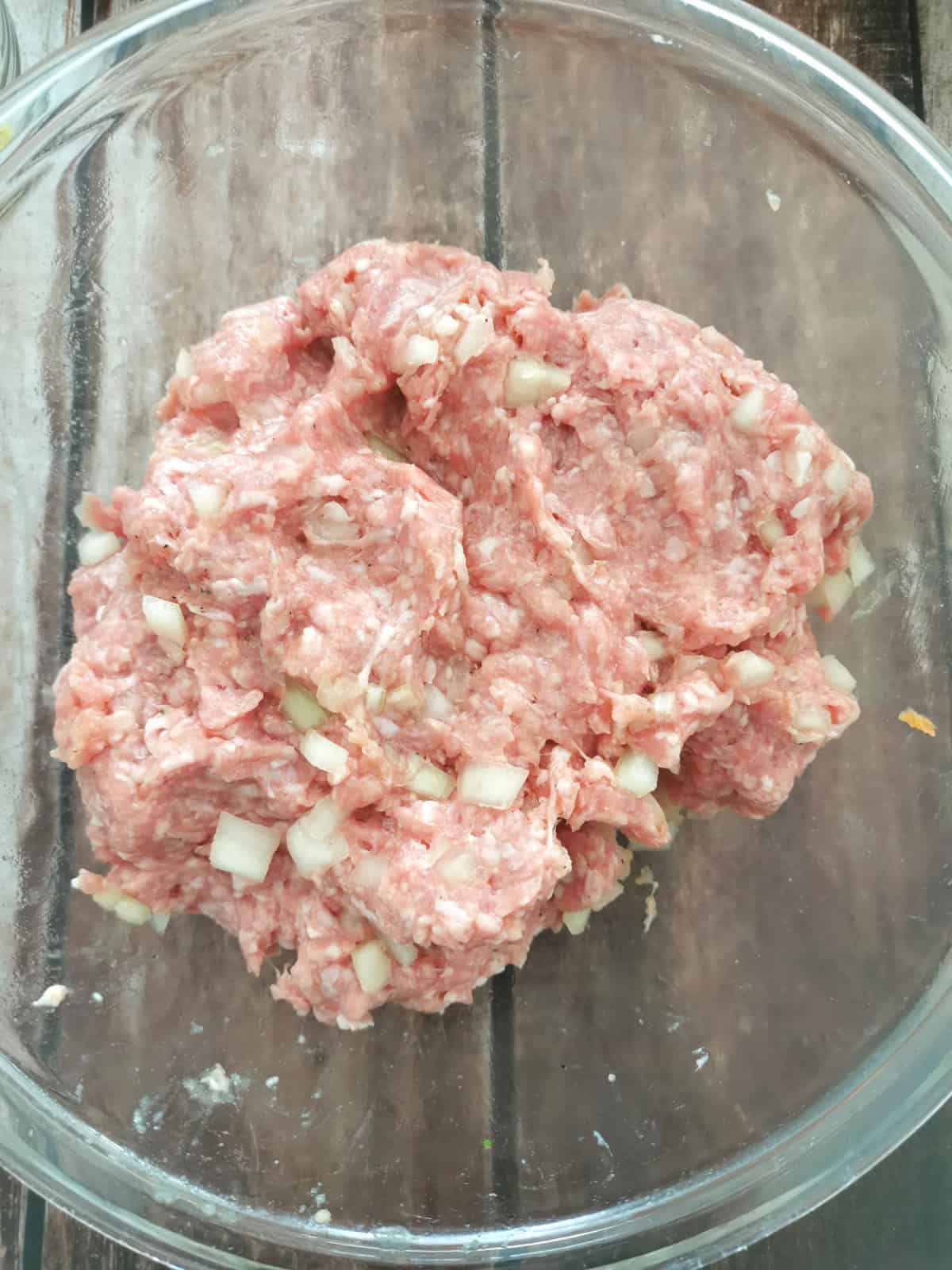 seasoned ground meat in large glass mixing bowl.