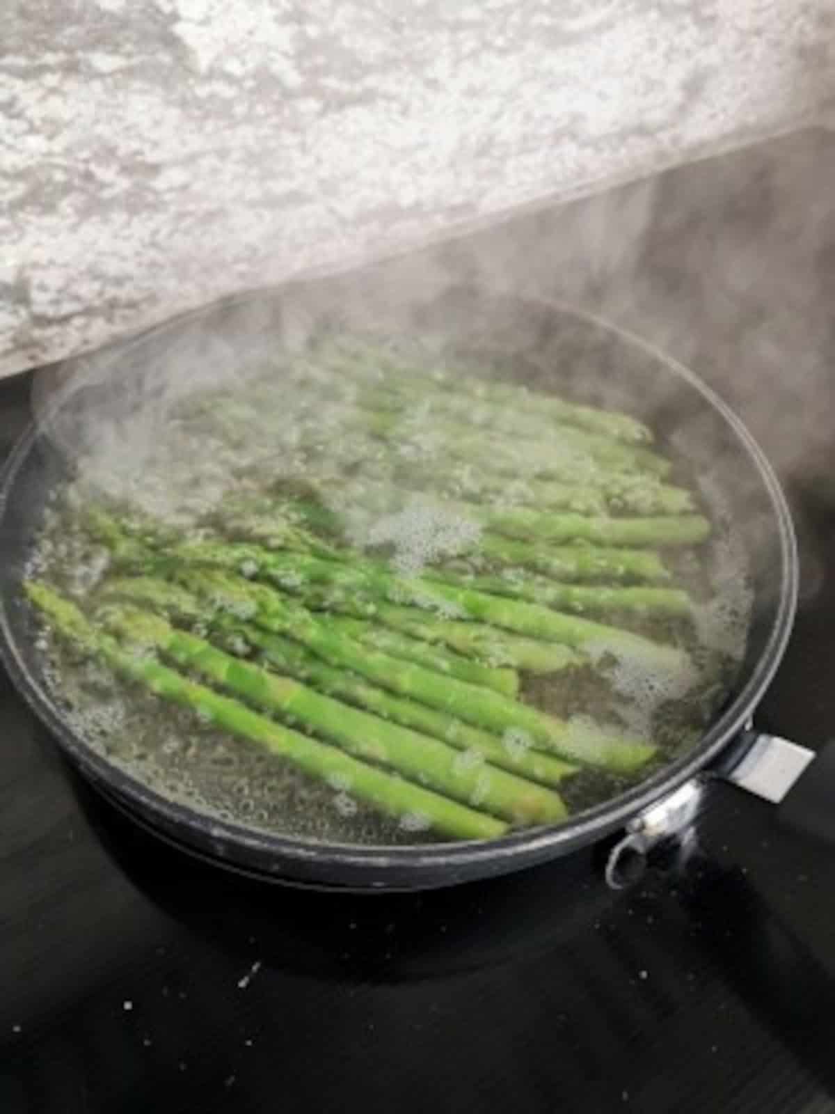asparagus cooking in boiling water in a pan on a stove.