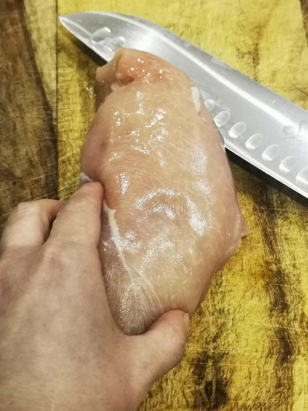 raw chicken breast on a cutting board with knife on the side.