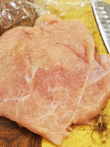 raw butterflied chicken on a cutting board with knife on the side.