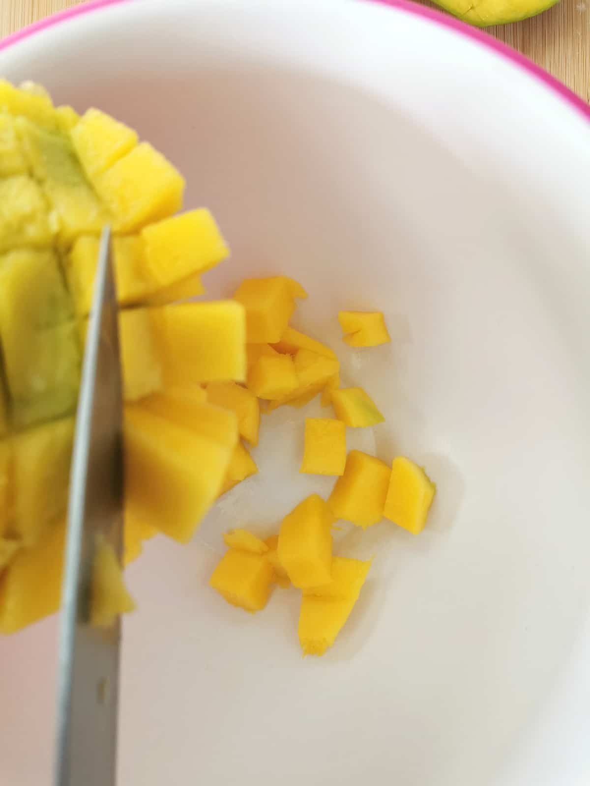 knife slicing cut up mango pieces from mango skin.