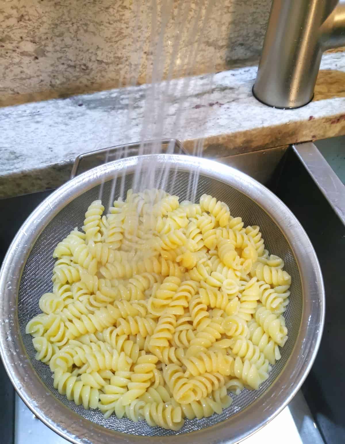 cooked pasta rinsing in a strainer in the sink under cool water.