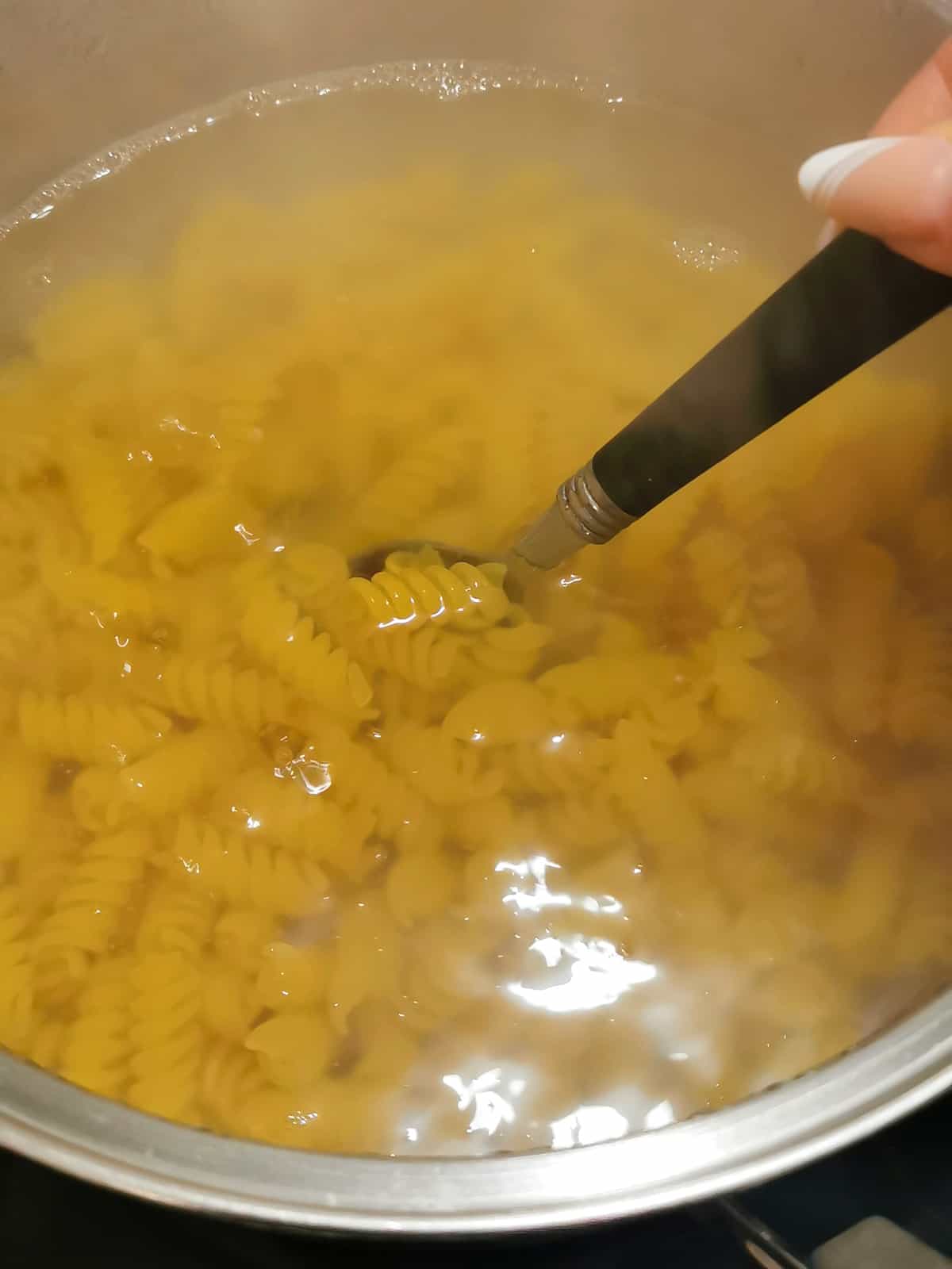 pasta cooked in boiling water in a large pot with spoon stirring the pasta.