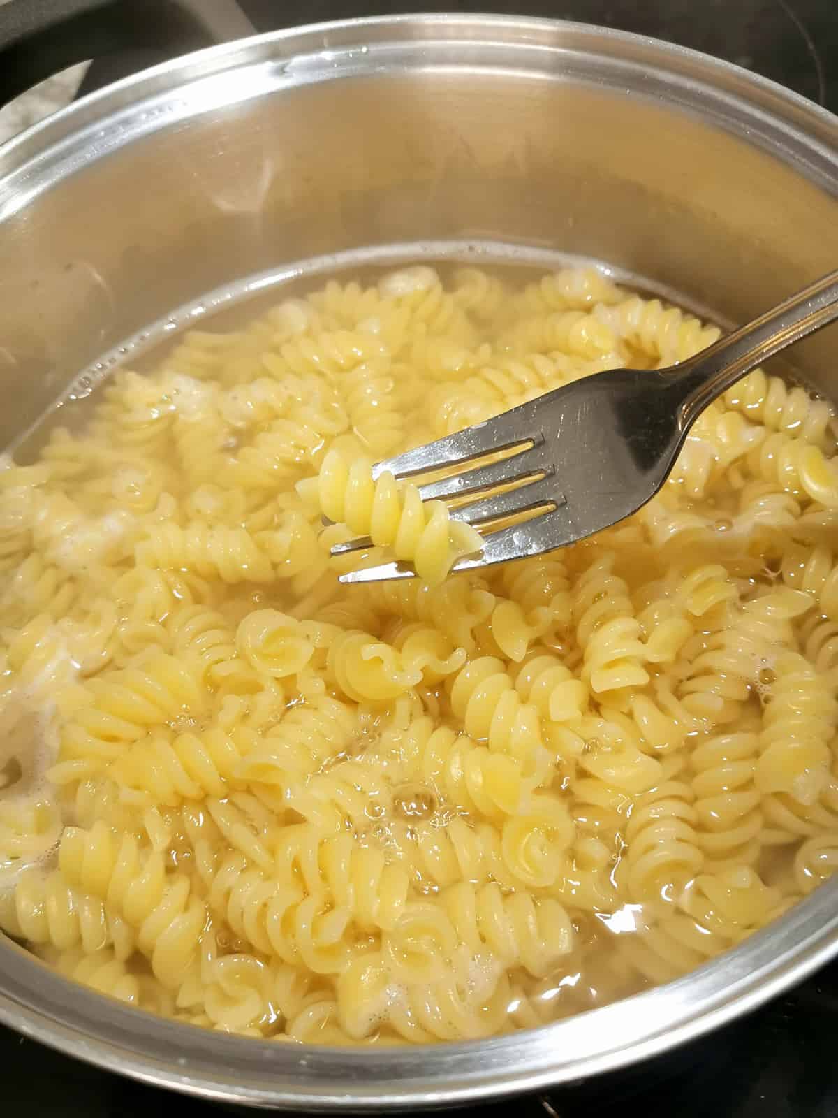 pasta cooked in boiling water in a large pot, with one pasta piece on a fork.