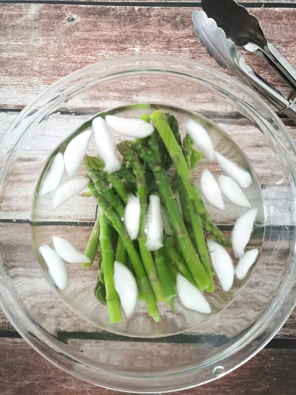 blanched asparagus in a large mixing bowl filled with cold water and ice.