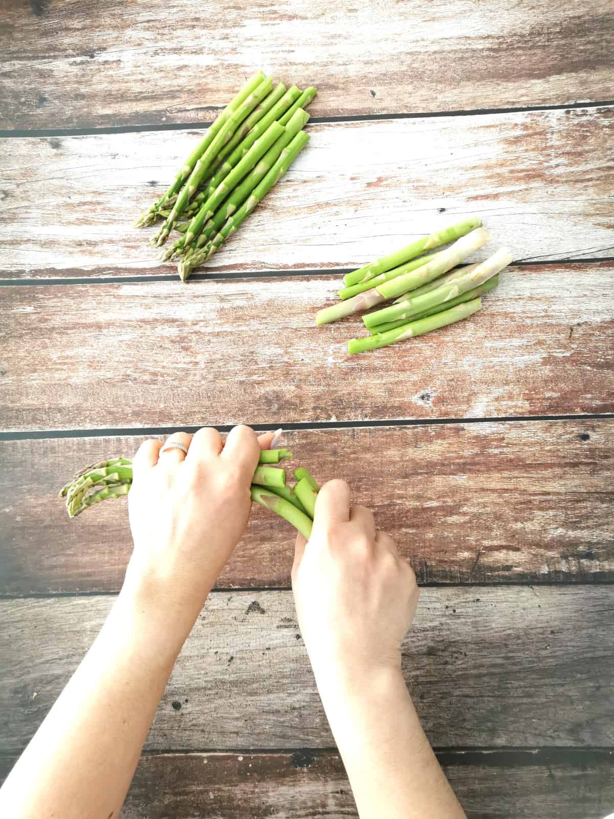 two hands snapping off the ends of asparagus spears.