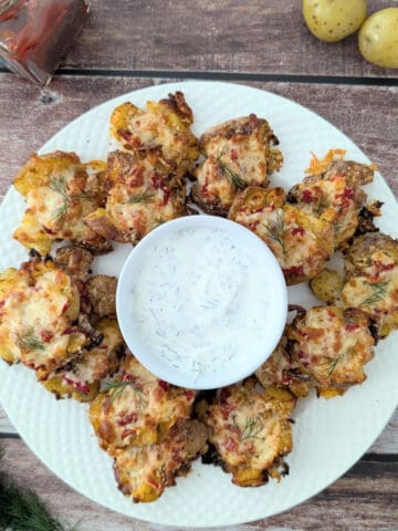 cheesy smashed potatoes with roasted red pepper on large white plate with sour cream dip.