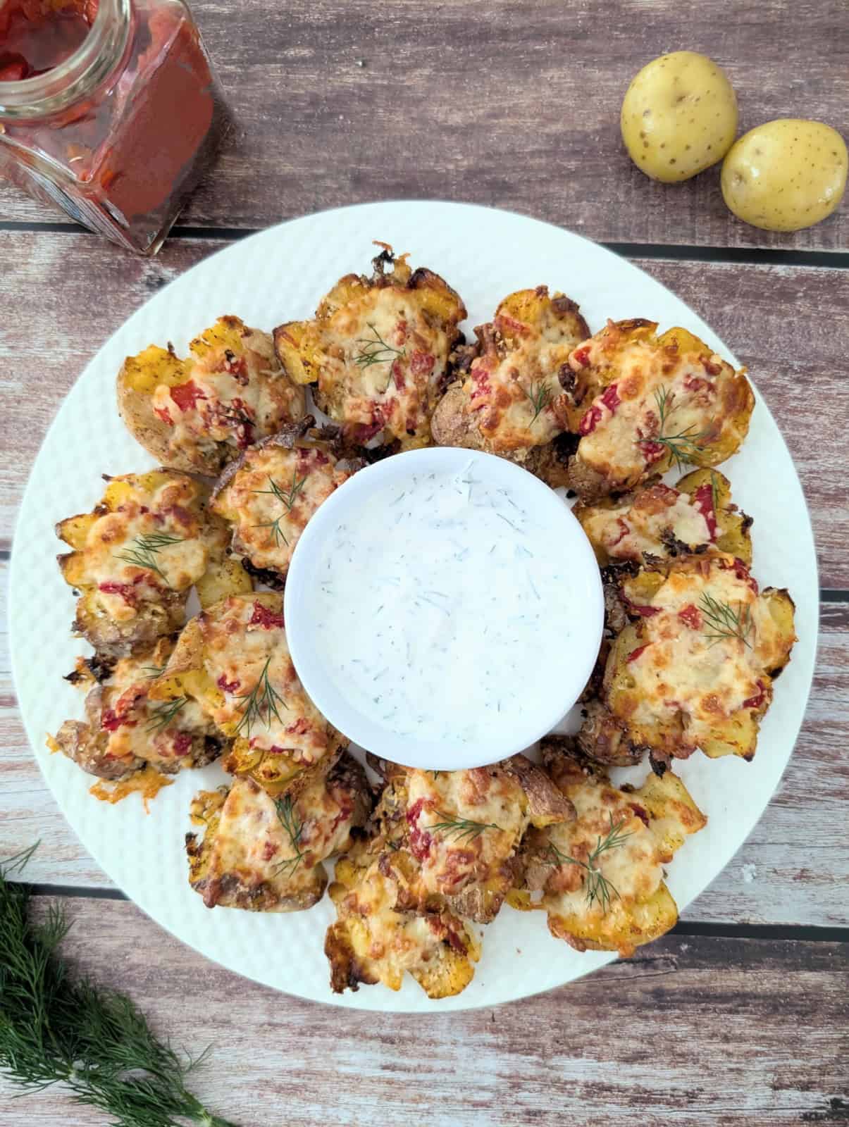 cheesy smashed potatoes with roasted red pepper on large white plate with sour cream dip.