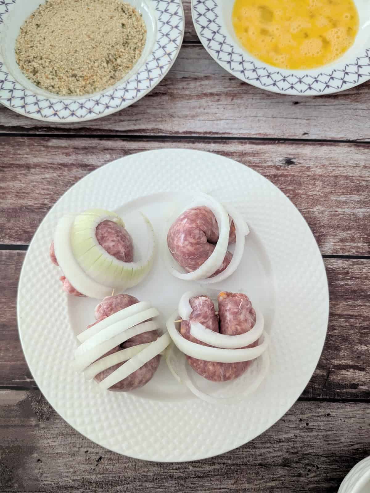 sausages wrapped with onions on a white plate.