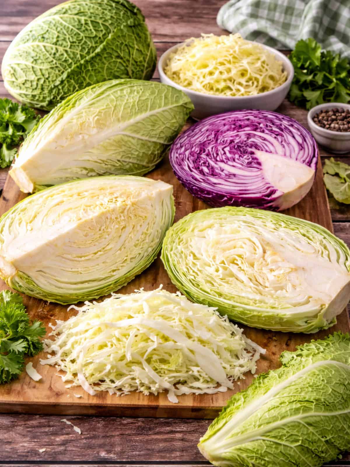 Different types of cabbage including green, savoy, napa, pointed, and red cabbage arranged on a wooden cutting board.