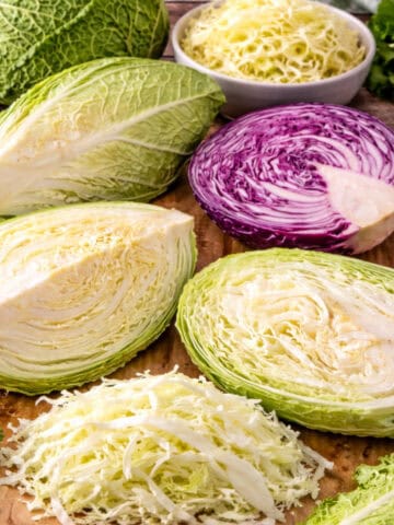 Different types of cabbage including green, savoy, napa, pointed, and red cabbage arranged on a wooden cutting board.