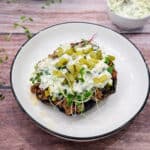 Ground beef stuffed portobello mushrooms with creamy sauce on a white plate with sauce on the side.