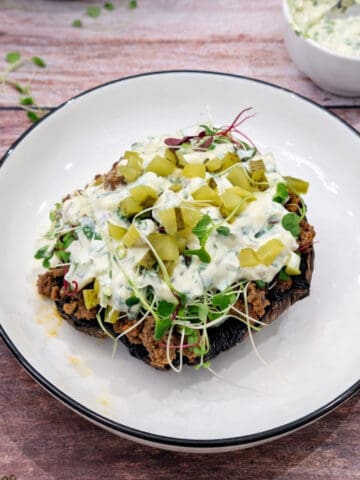 Ground beef stuffed portobello mushrooms with creamy sauce on a white plate with sauce on the side.