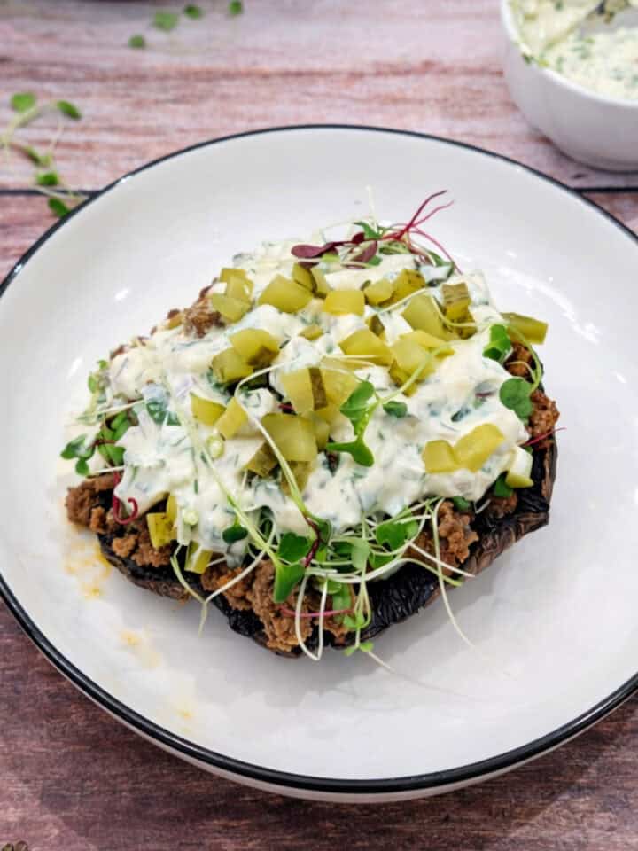 Ground beef stuffed portobello mushrooms with creamy sauce on a white plate with sauce on the side.