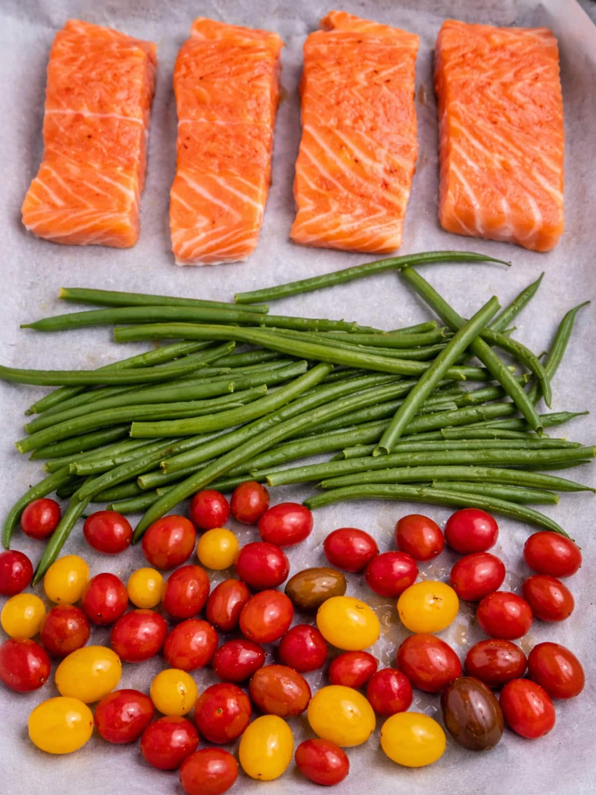 Raw salmon fillets with green beans and cherry tomatoes on a sheet pan.