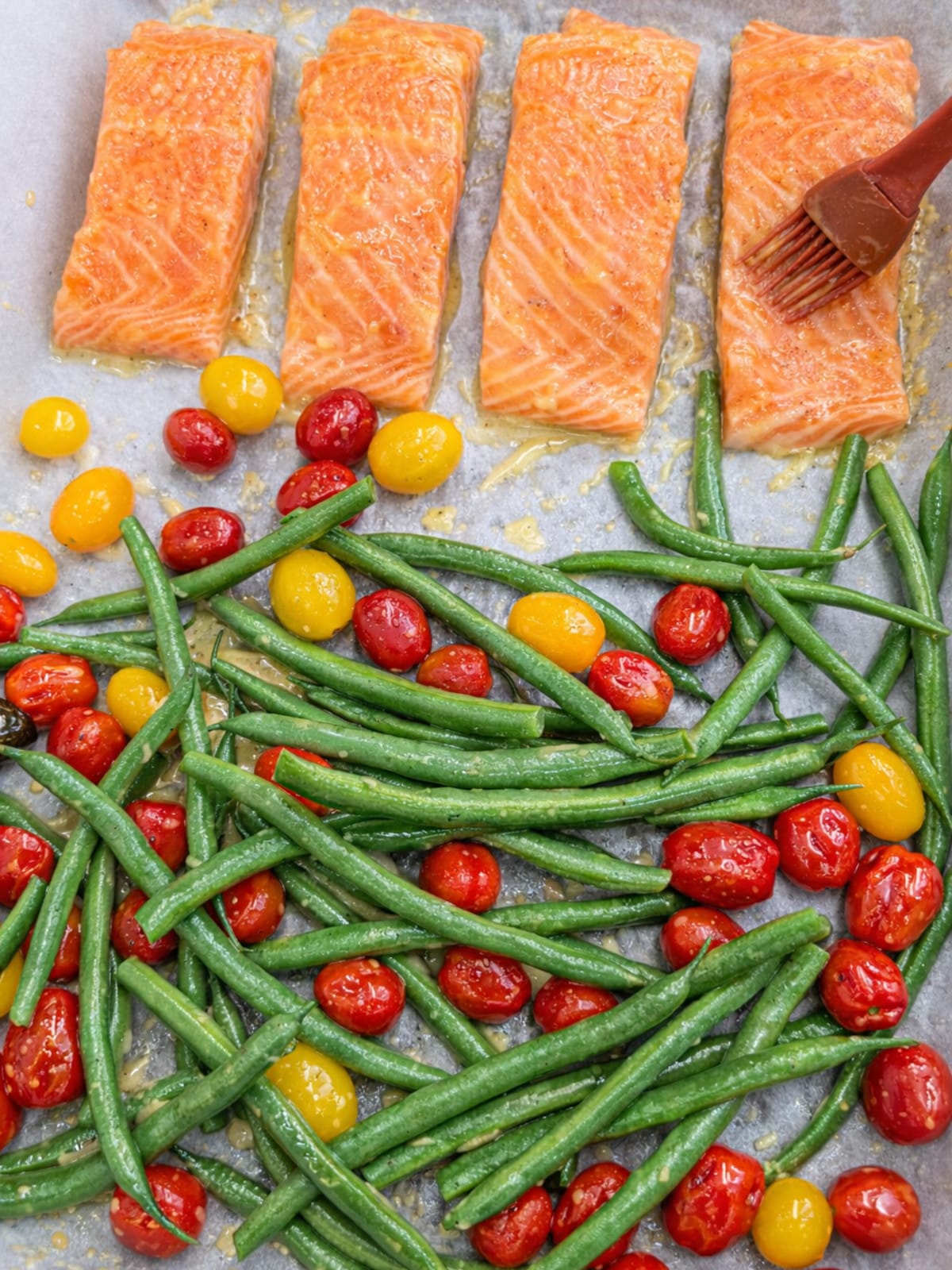 Seasoned salmon fillets with green beans and tomatoes with ruber brush brushing sauce, ready for baking.