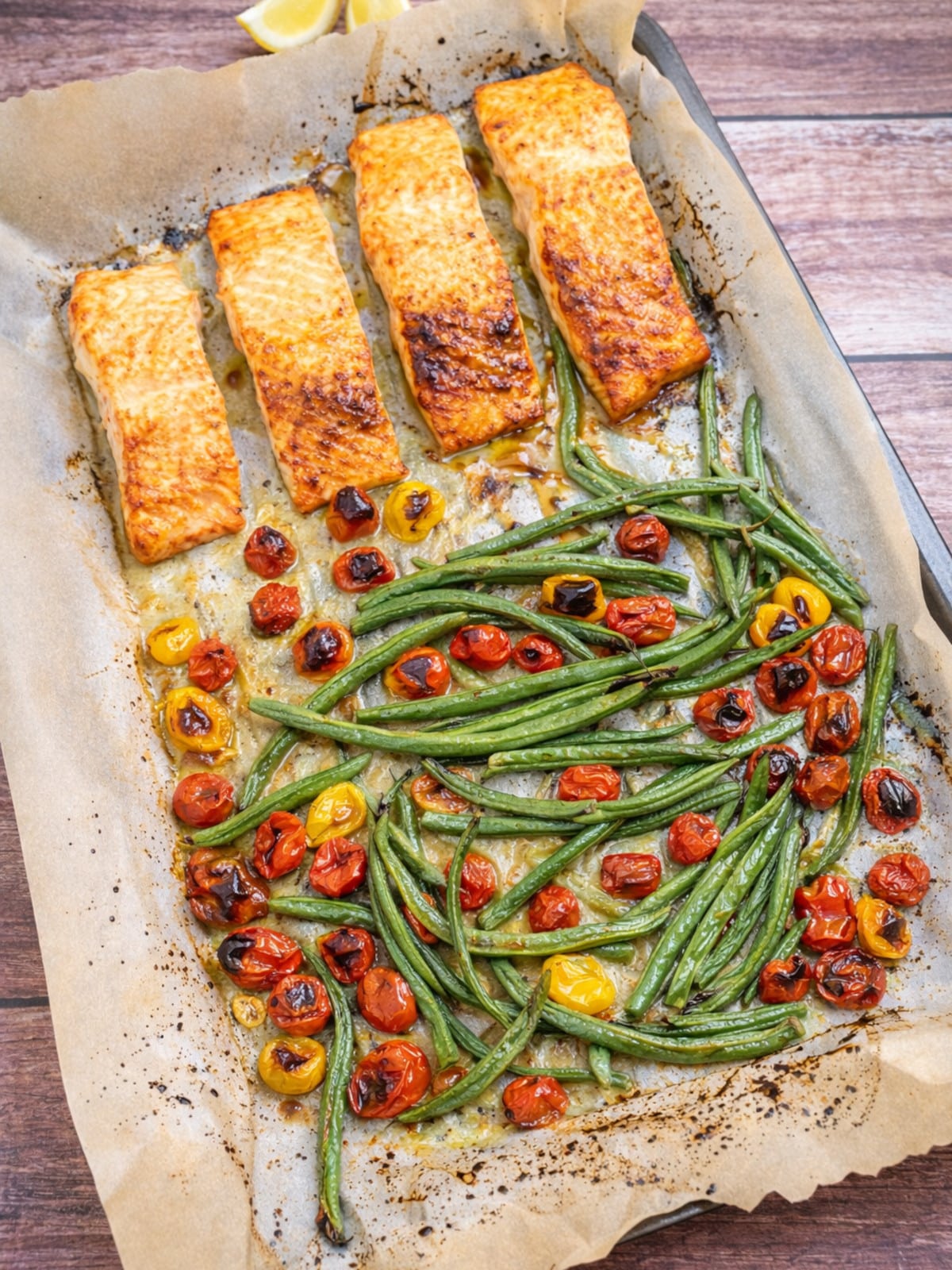 fully baked salmon with aked green beans and cherry tomatoes on a baking sheet.