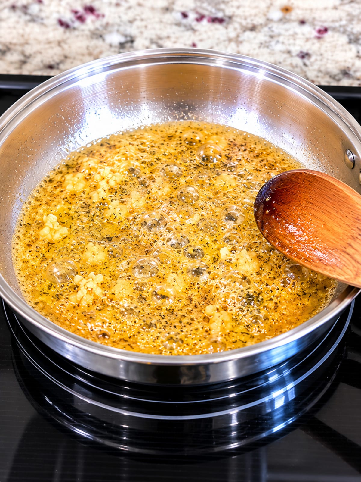 Garlic butter sauce simmering in skillet with minced garlic and herbs.