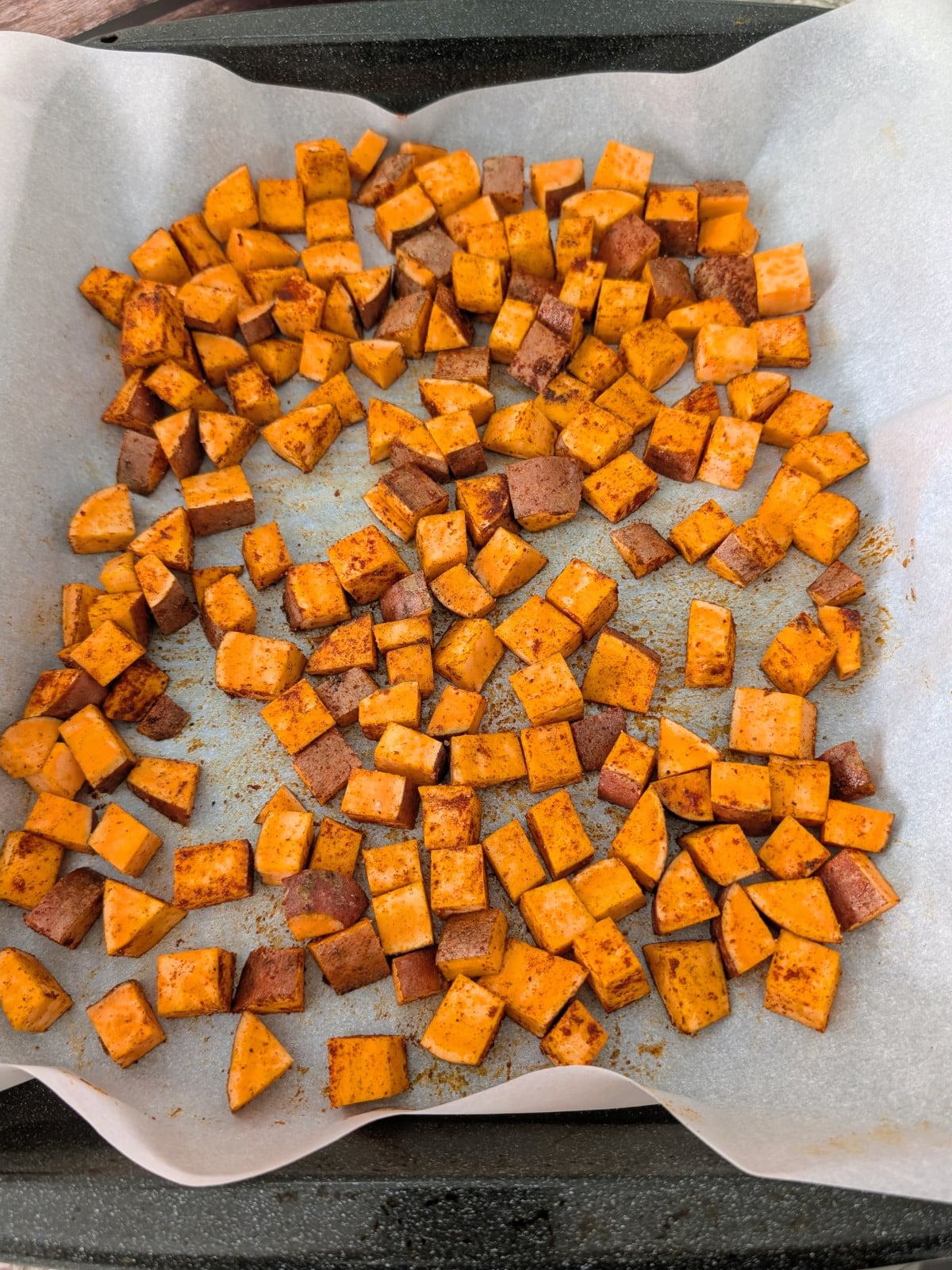 Seasoned and cubed sweet potatoes on a parchment paper lined baking sheet.