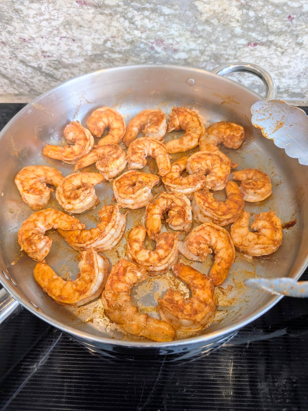 seasoned chili lime shrimp cooking in a stainless steel skillet on the stove.