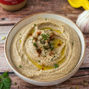 creamy lentil dip with tahini in a bowl garnished with paprika and parsley.
