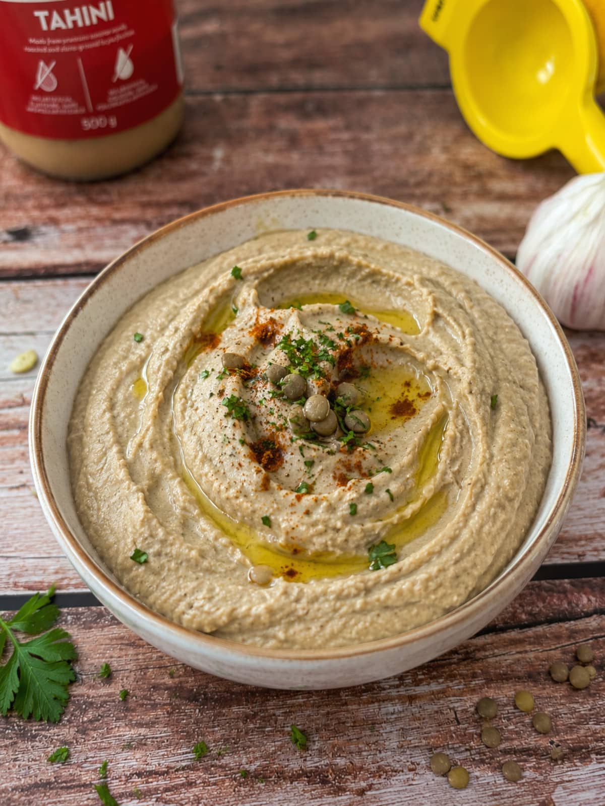 creamy lentil dip with tahini in a bowl garnished with paprika and parsley.