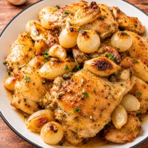Easy oven baked chicken thighs served with roasted garlic and caramelized pearl onions in a buttery herb sauce.