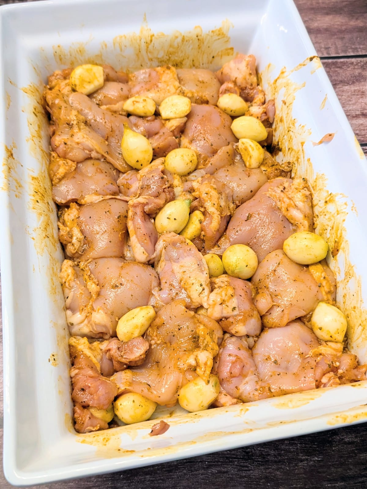 Chicken thighs coated in butter herb sauce with whole garlic cloves and pearl onions before baking.