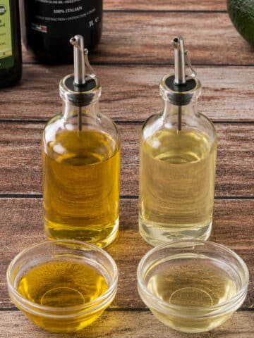Side-by-side comparison of dark and light cooking oils in clear glass dispensers and bowls, illustrating the difference between cold-pressed and expeller-pressed oils.